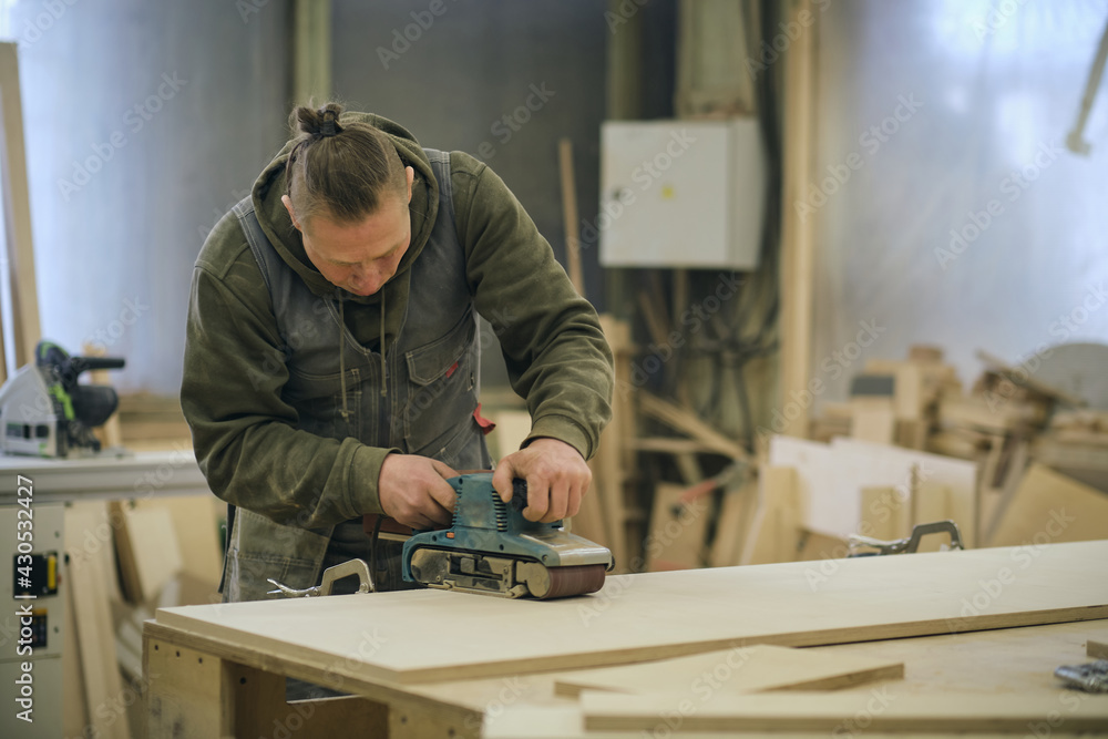 Close up. Carpenter at workshop polishes wooden board with a electric orbital sander. Woodwork and furniture making concept. Close up. Carpenter at workshop polishes wooden board with a electric orbital sander. Woodwork and furniture making concept.