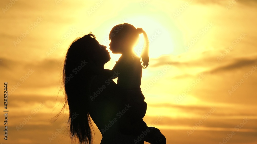 Happy mother and little child are playing, hugging in park on nature in rays of sun. A happy family. Mom is circling her beloved daughter in her arms. Mom and baby silhouette, childhood, motherhood