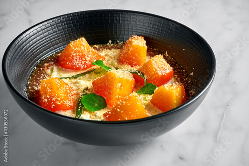 An appetizing and unusual Italian dessert - Stracciatella di bufala with persimmon and jam, served in a black plate on a marble background.