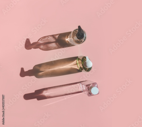 Three cosmetic product bottles in sunlight with shadow on pink background. Top view