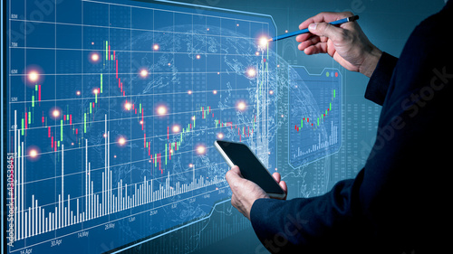 Fototapeta Naklejka Na Ścianę i Meble -  A man wearing a suit on his left hand holding a cell phone His right hand poked a pencil on a simulation fast-growing stock chart. Globe background and blurred lights