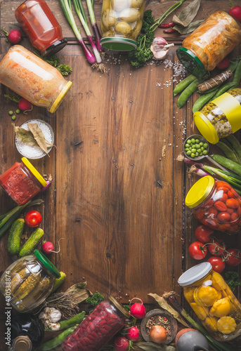 фотографія Frame of various pickled colorful vegetables in jars on wooden background with ingredients, herbs and spices