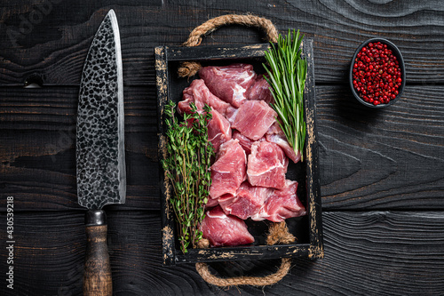 Raw Diced pork cubs meat with spices in a rustic tray. Black wooden background. Top view photo