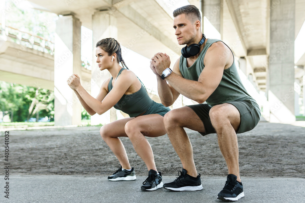 Fototapeta premium Athletic couple doing squats during street workout