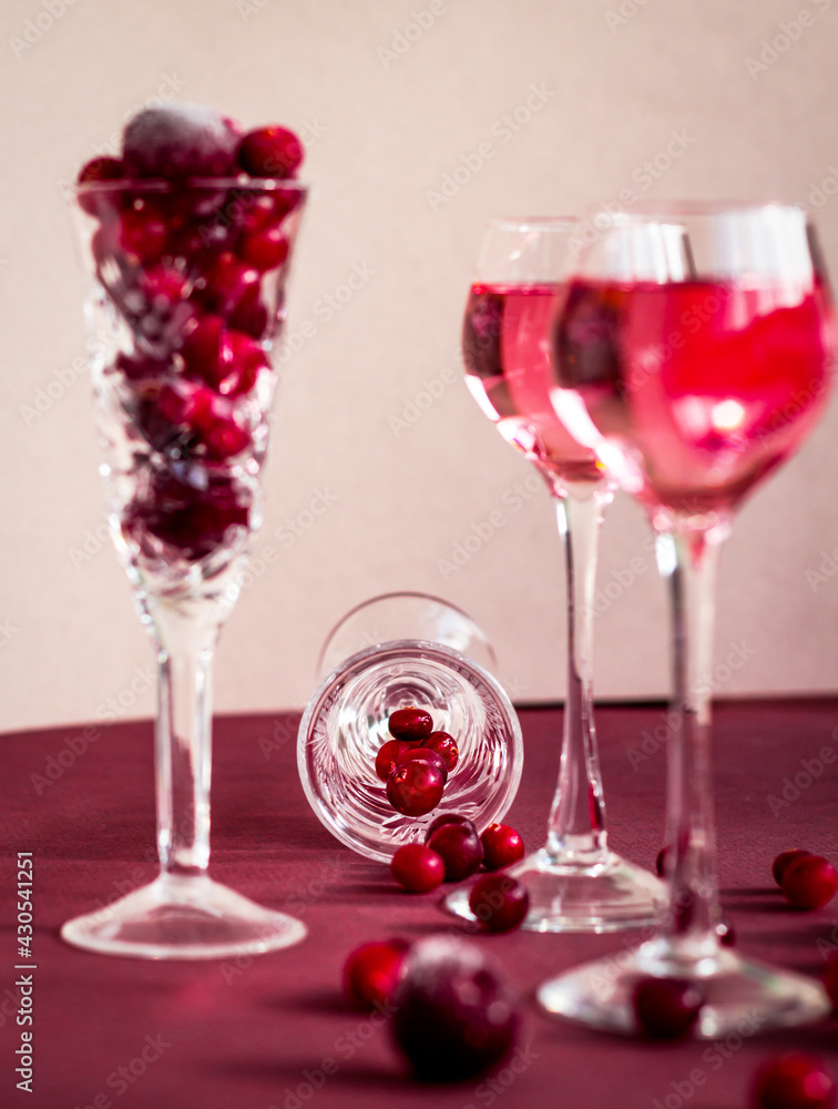 red berries scattering from a crystal glass lying on the table among glasses with pink alcoholic drink, many cranberries and cherries on crystal wine glass red berries scattering from a crystal glass lying on the table among glasses with pink alcoholic drink, many cranberries and cherries on crystal wine glass