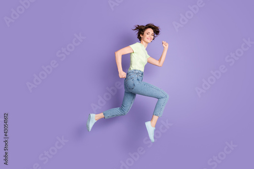 Full length body size profile side view of lovely cheerful sporty girl jumping running marathon isolated over violet color background