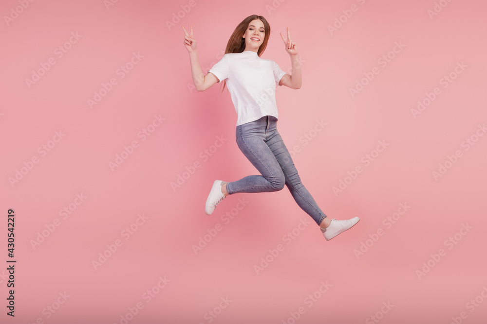 Photo of active girl jump high up run show peace gesture on pink background Photo of active girl jump high up run show peace gesture on pink background
