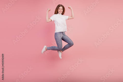 Photo of active girl jump high up raise fists wear casual clothes on pink background