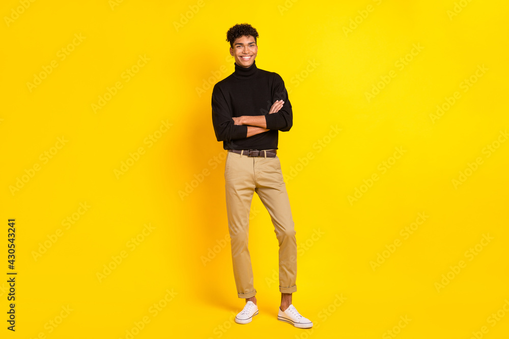 Full size photo of optimistic brunet guy stand crossed arms wear black sweater trousers sneakers isolated on yellow color background Full size photo of optimistic brunet guy stand crossed arms wear black sweater trousers sneakers isolated on yellow color background