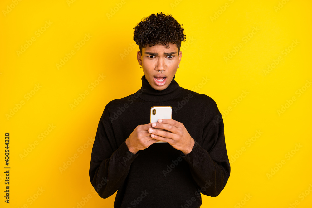 Photo of upset shocked dark skin man wear black sweater looking modern gadget isolated yellow color background Photo of upset shocked dark skin man wear black sweater looking modern gadget isolated yellow color background