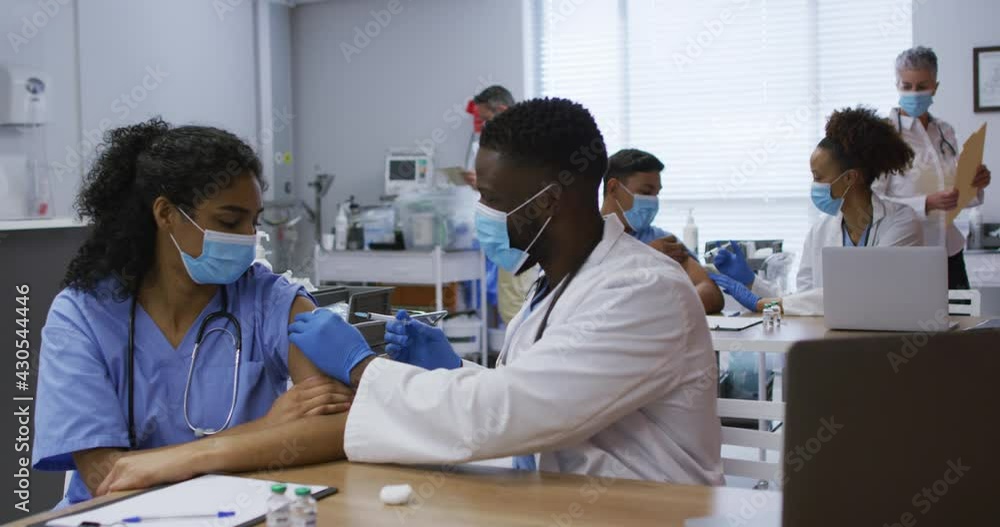 African american male doctor giving covid vaccination to female colleague, both in face masks African american male doctor giving covid vaccination to female colleague, both in face masks