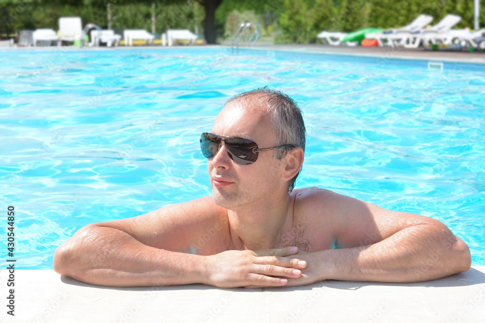 Close-up portrait of a young attractive man in sunglasses at the edge of the pool.Recreation, sports, travel