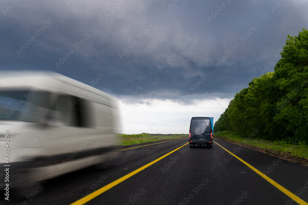 Bacl of delivery small shipment cargo courier van moving fast on wet highway road to city urban suburb against rainy cloudy sky . Business distribution and logistics express service. Mini bus motion
