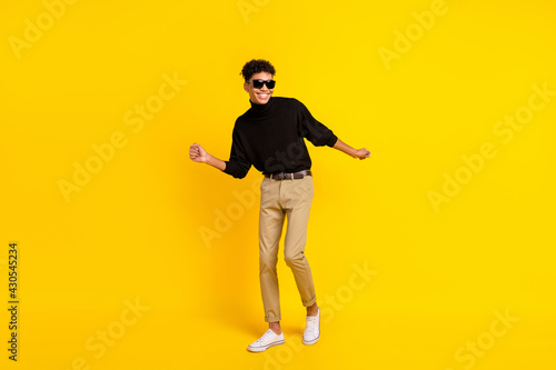 Full size photo of optimistic nice brunet guy dance wear spectacles black sweater trousers sneakers isolated on yellow background