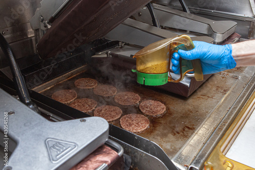 The burger patties are grilled. Salting and peppering food while frying.  cooking in a restaurant