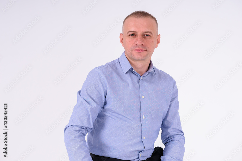 A man in a blue shirt and black trousers sits on a stool on a white background A man in a blue shirt and black trousers sits on a stool on a white background