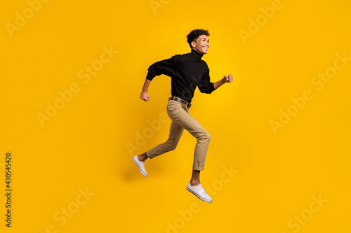 Full size profile photo of optimistic nice brunet guy run wear black sweater trousers sneakers isolated on yellow background