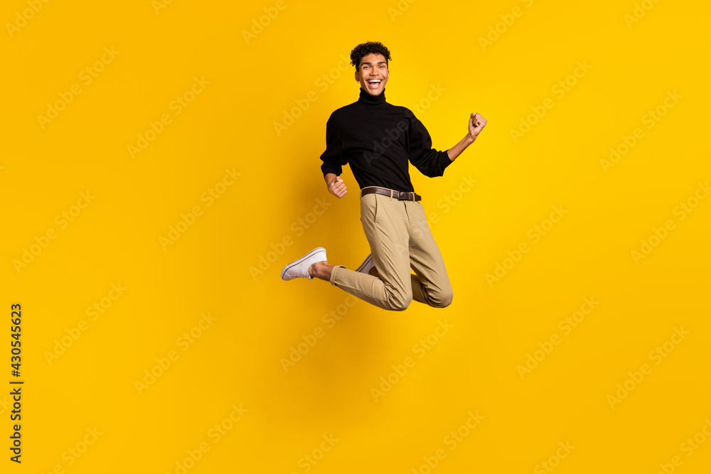 Photo of funny lucky dark skin guy dressed black pullover jumping rising fists isolated yellow color background
