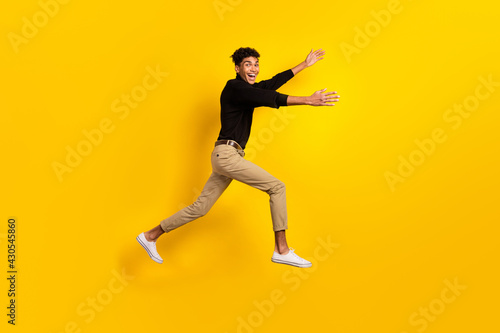 Photo of funny charming dark skin guy dressed black pullover jumping running open arms isolated yellow color background