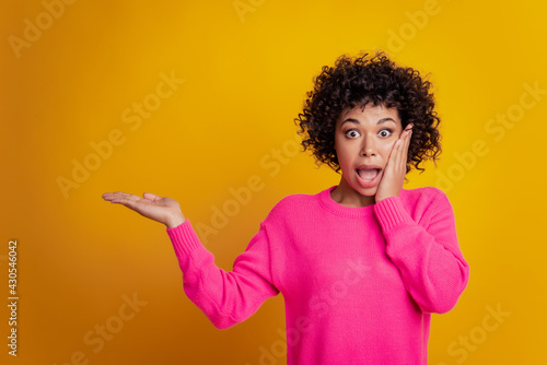 Young excited amazed woman isolated yellow background palm holding copyspace open mouth