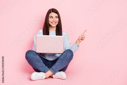 Full size photo of nice optimistic brunette hairdo lady sit type laptop point empty space wear shirt jeans isolated on pink background