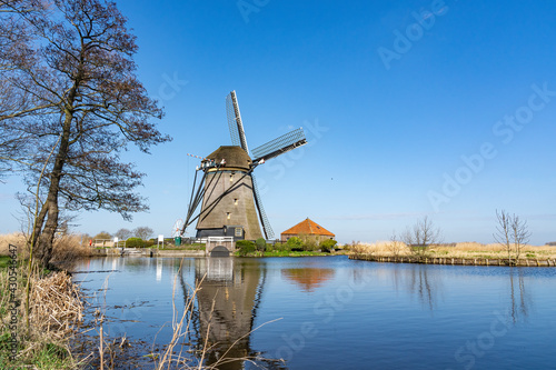 Photo of a stately old windmill under a clear blue sky with reflection in the Kerkvaart near Hazerswoude village, the Netherlands photo