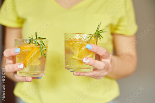 Female woman hand hold two glasses of citrus orange and rosemary fresh lemonade