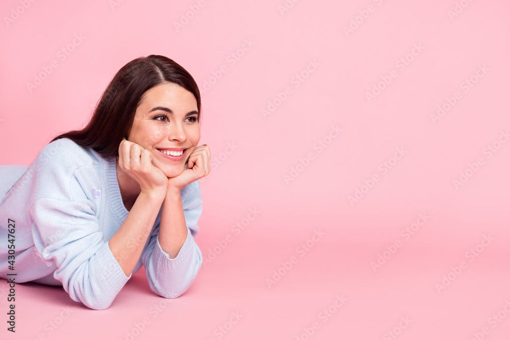 Photo of shiny pretty young lady dressed blue sweater lying floor arms cheeks chin looking empty space isolated pink color background Photo of shiny pretty young lady dressed blue sweater lying floor arms cheeks chin looking empty space isolated pink color background