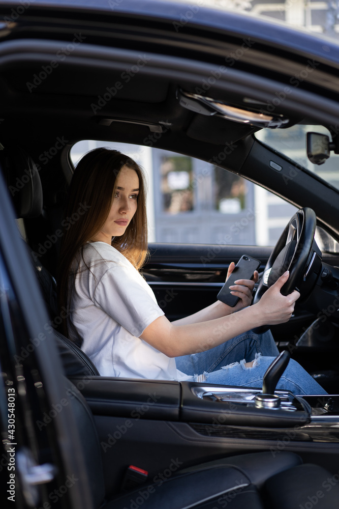 The model is sitting in the car and looking at the road. In the hands of the girl's phone.