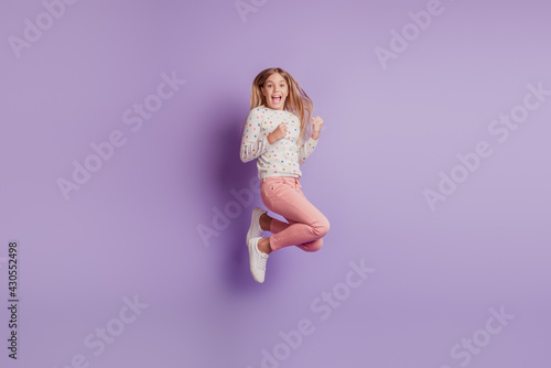 Young kid girl win victory jump up over violet background