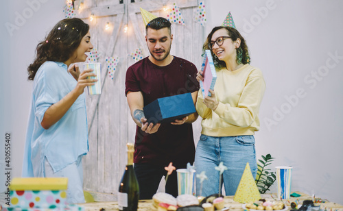 Young hipsters greeting girl on her birthday party opening decorative box with surprise during celebration  happy young woman amazed with gift from best friends satisfied with holiday and festive mood