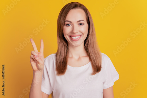 Young girl show victory sign isolated on yellow background