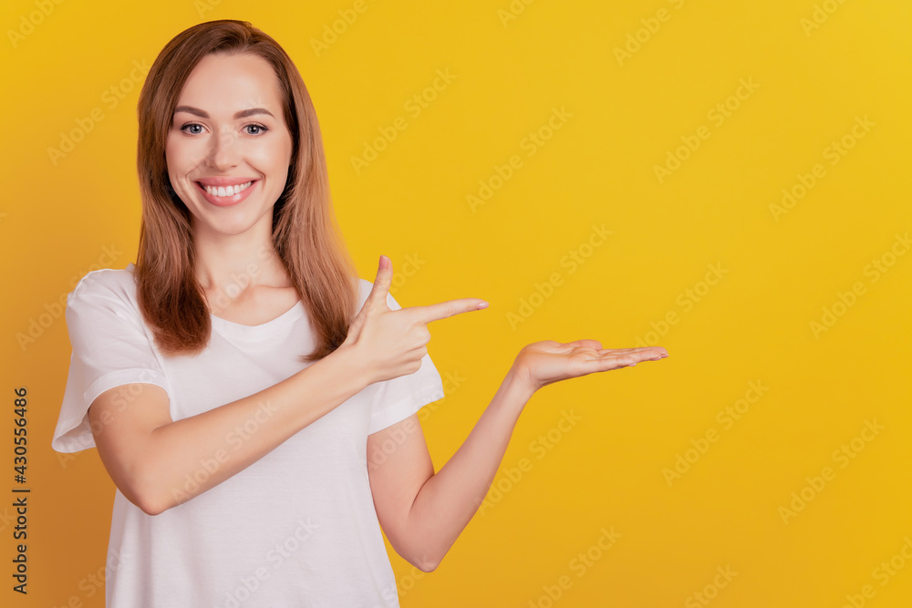 Young promoter woman direct forefinger empty space hold palm toothy smile on yellow wall Young promoter woman direct forefinger empty space hold palm toothy smile on yellow wall