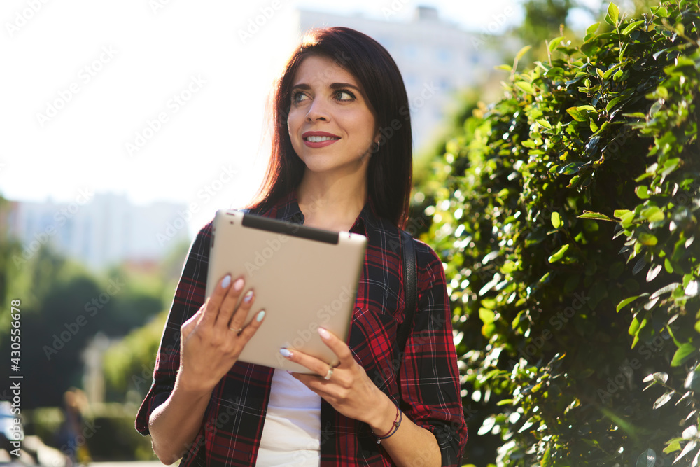 Pretty female with modern touch pad technology thinking about travel vacations during sunny summer daytime, attractive Caucaisan blogger using digital tablet with 4g internet spending leisure in city Pretty female with modern touch pad technology thinking about travel vacations during sunny summer daytime, attractive Caucaisan blogger using digital tablet with 4g internet spending leisure in city