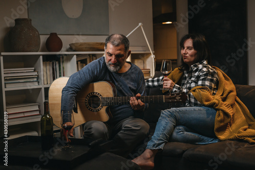 middle age couple drinking wine at home. man playing acoustic guitar