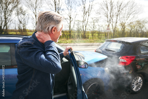 Senior Male Driver With Whiplash Injury Getting Out Of Car After Traffic Accident