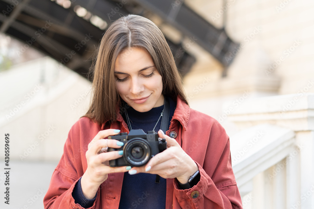 Close up of a cahrming brunet woman checking her fresh made picture on the camera standing outside in the modern street