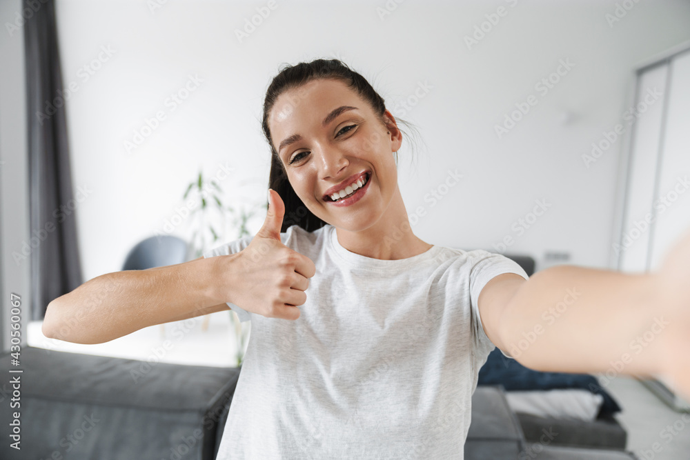 Naklejka premium Smiling brunette woman showing thumb up while taking selfie photo