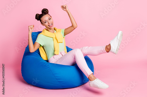 Photo of pretty lucky young woman wear green t-shirt sitting beanbag rising fists isolated pink color background