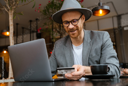 White bearded man using laptop and credit card in cafe outdoors