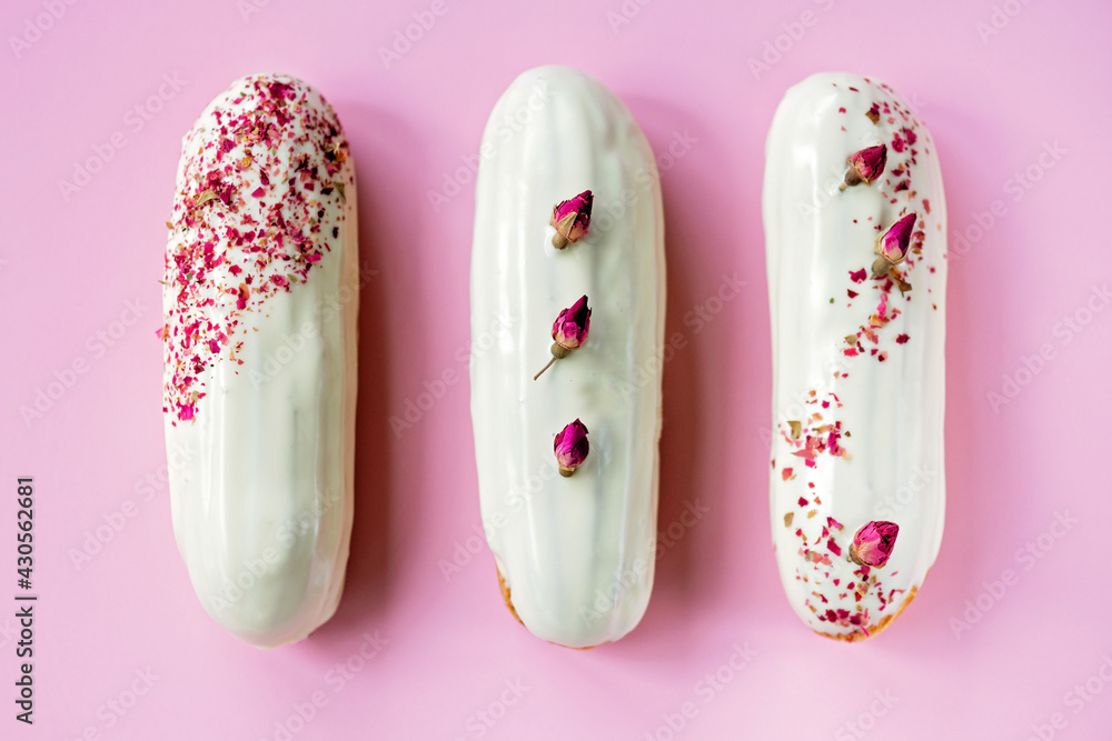 French dessert eclairs or profiteroles with rose-flavored white chocolate glaze, on a pink background. Pastry cakes with custard, rose cream and topping. Soft selective focus. French dessert eclairs or profiteroles with rose-flavored white chocolate glaze, on a pink background. Pastry cakes with custard, rose cream and topping. Soft selective focus.