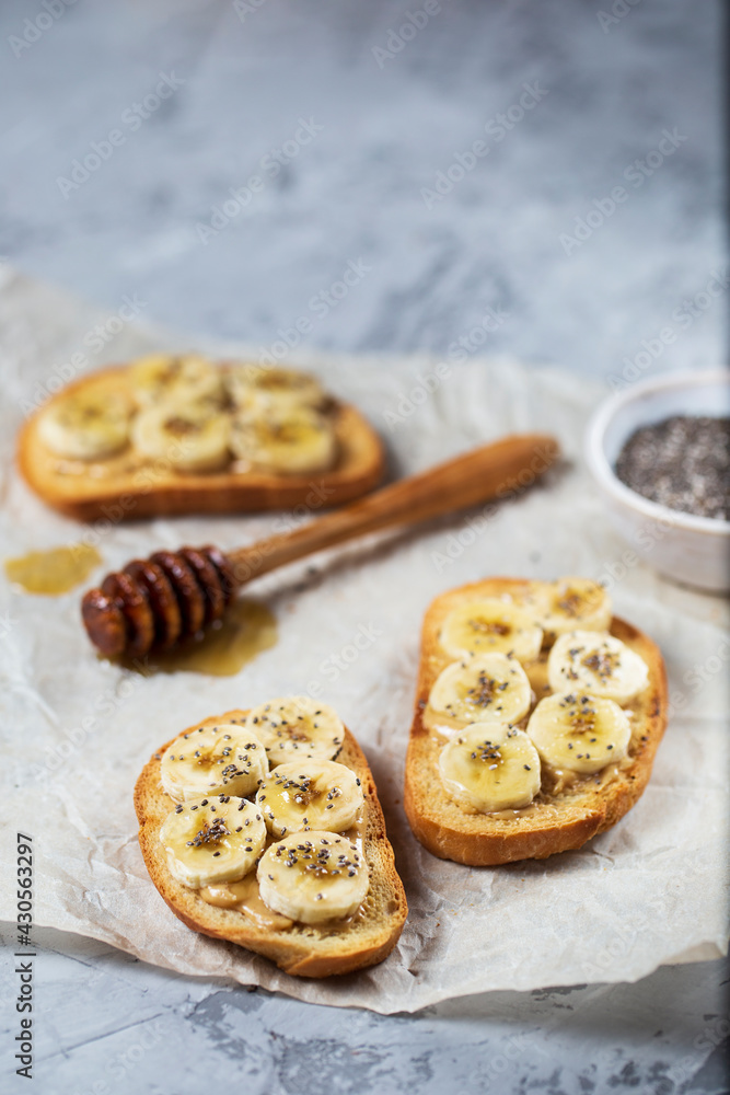 Delicious toasted sandwich bread with peanut butter, banana, honey, chia seeds on concrete background. Healthy, balanced traditional American school breakfast. Vegan sweet dessert. Delicious toasted sandwich bread with peanut butter, banana, honey, chia seeds on concrete background. Healthy, balanced traditional American school breakfast. Vegan sweet dessert.