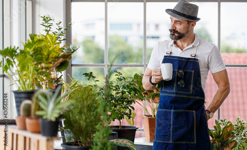 A beautiful bearded man wearing hat holding a coffee cup and walk in his indoor home garden in the happy and calm manner