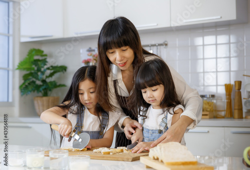 Beautiful and cute Asian mother teaching and showing the 2 daughters, 3 years and 7 years old, how to cut and slice bread