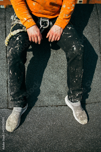 Tired and dirty industrial climber have rest on the roof after work and enjoying the sun. Close up of dirty work pants. Worker outside. 
