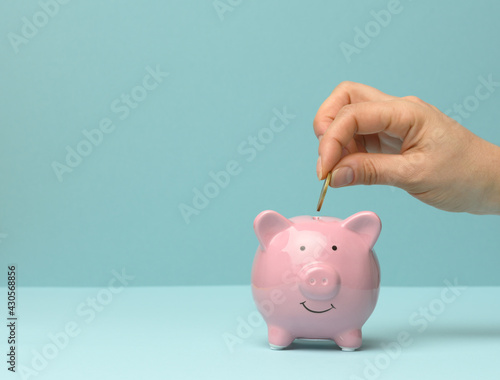ceramic pink piggy bank and hand throwing a coin inside, finance savings concept