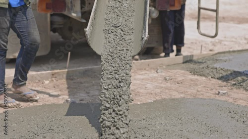 Workers are spreading the concrete that flows and pouring from a cement mixer truck, pouring liquid concrete into the roadway at the construction site.