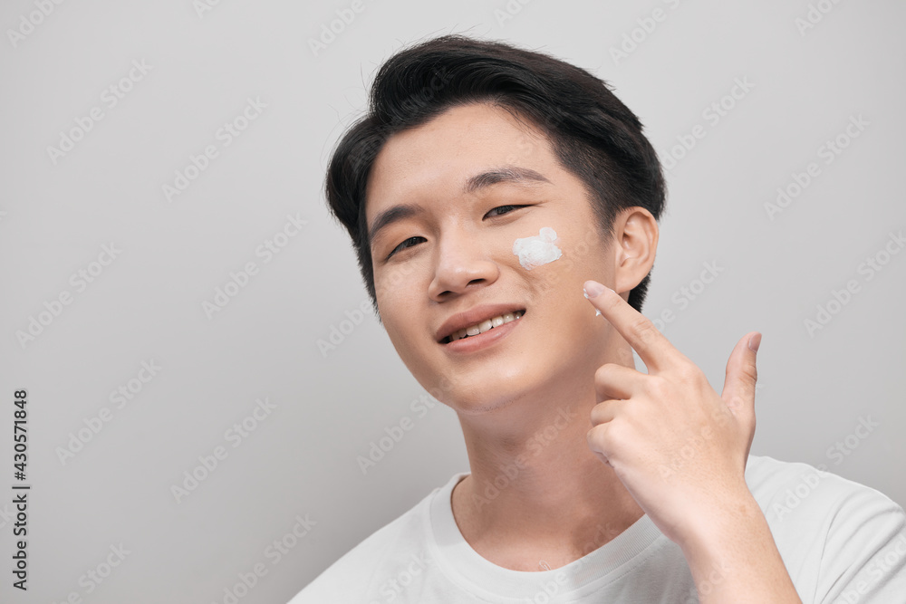Skin care. Portrait of handsome young man applying cream to his face, isolated on white background Skin care. Portrait of handsome young man applying cream to his face, isolated on white background