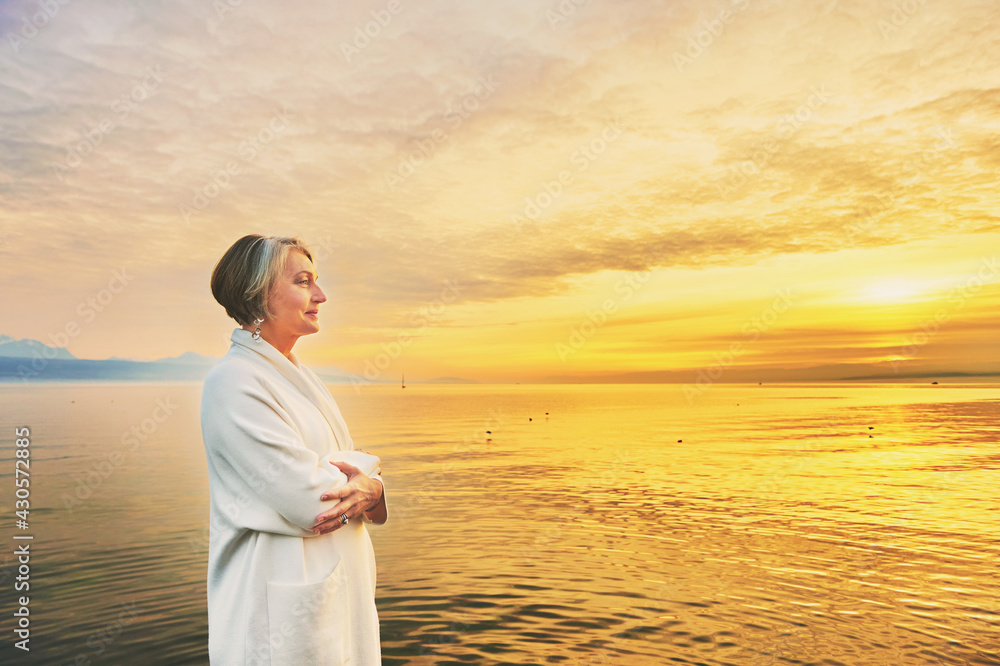 Beautiful middle age woman admiring amazing view of lake at sunset Beautiful middle age woman admiring amazing view of lake at sunset