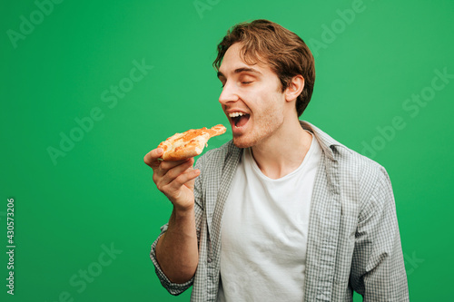 Nice man bites piece of pizza  isolated on green background